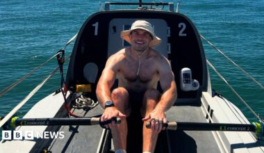 Olly Rathbone, in a cream-coloured wide-brimmed boonie hat, rows a boat before attempting to cross the Atlantic