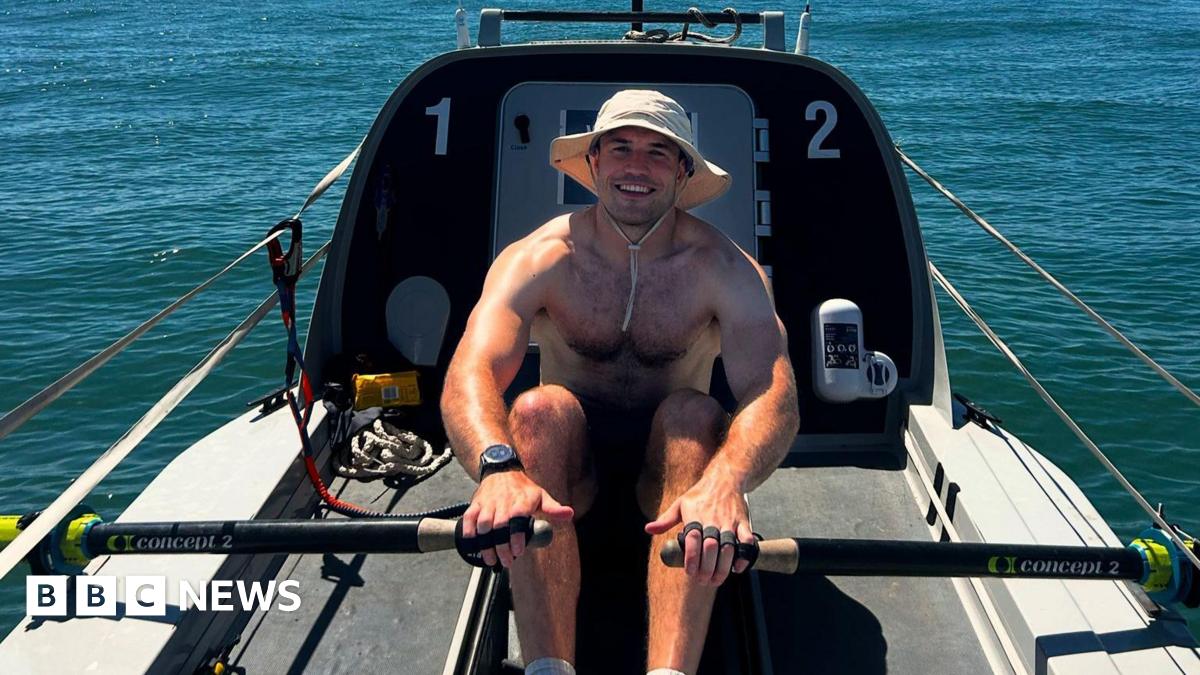 Olly Rathbone, in a cream-coloured wide-brimmed boonie hat, rows a boat before attempting to cross the Atlantic
