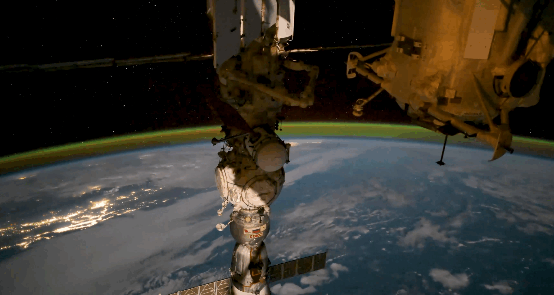 a green glow floats above earth in the background as a cylindrical space station module dominates the foreground