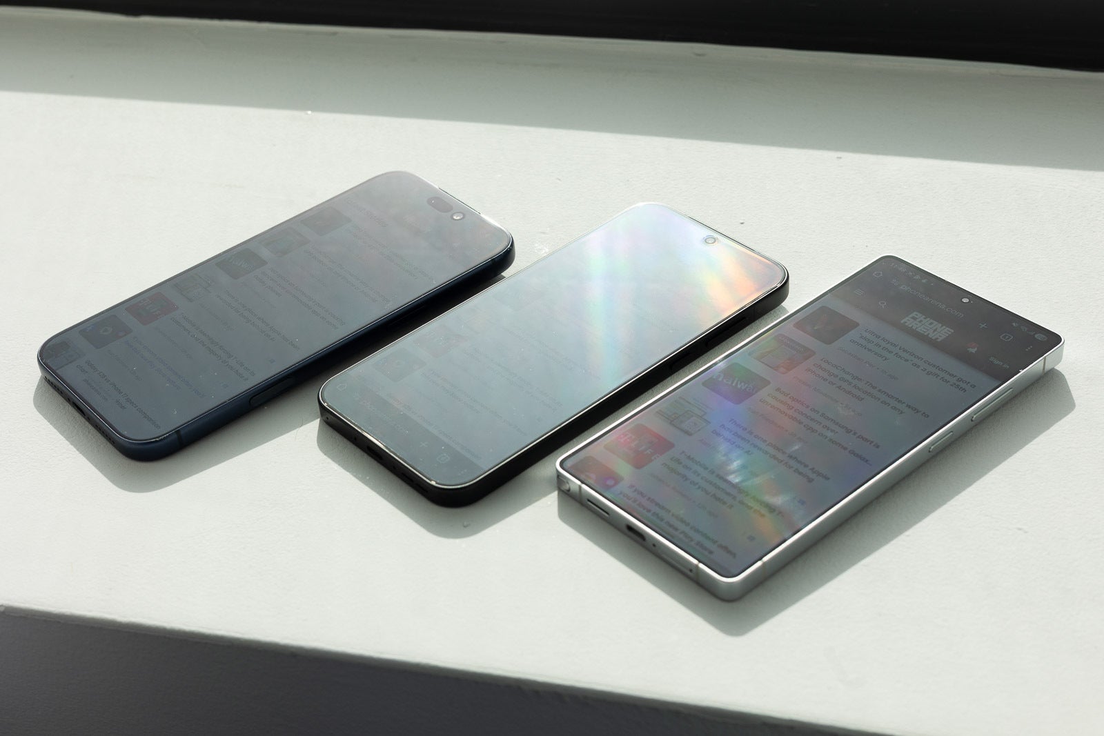 Phones on a windowsill in direct sunlight showing strong screen glare.