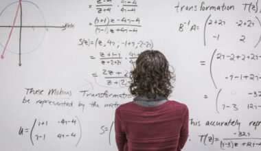 A woman standing in front of a white board that is packed with equations.