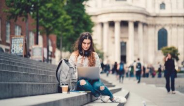 Female student sitting at the steps and using laptop