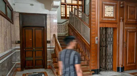 Getty Images A man walks past the lobby area of the Seksaria building, a Unesco-designated Art Deco apartment along the Marine Drive seafront in Mumbai. Inside the building are wooden doors, stairs and wall pannelling. Tile-work also features on the floor and walls. 