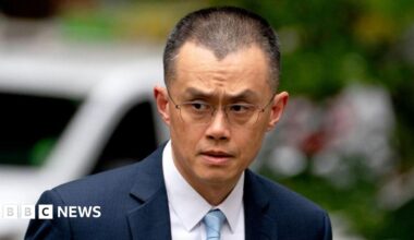 A close-up image of Changpeng Zhao, former chief executive officer of Binance, dressed in a dark blue suit and a light blue tie. He is pictured glancing towards his right as he arrives at a court in Seattle.