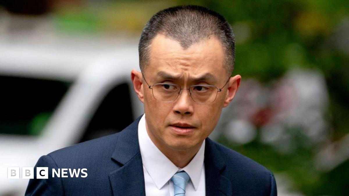 A close-up image of Changpeng Zhao, former chief executive officer of Binance, dressed in a dark blue suit and a light blue tie. He is pictured glancing towards his right as he arrives at a court in Seattle.