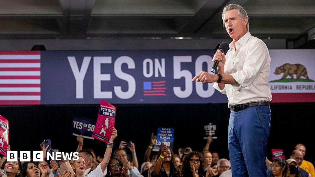 California Gov Gavin Newsom appears on stage in support of a redistricting effort in his state. People in the audience are holding up signs in support of Prop 50 and on the wall in the background is a "YES ON 50" sign.