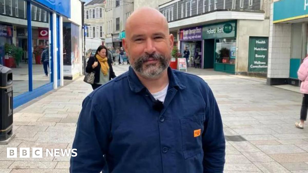 The two buildings which make up Trago Mills in Falmouth. One is wooden two-storey building and the other is a three-storey building along Arwenack Street. There is a hatched area in front of the wooden building and it has the nations' flags flying.
