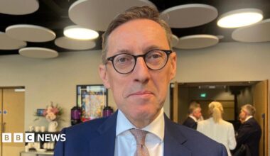 Deputy Ian Gorst is wearing a blue suit and white shirt with a pink tie.