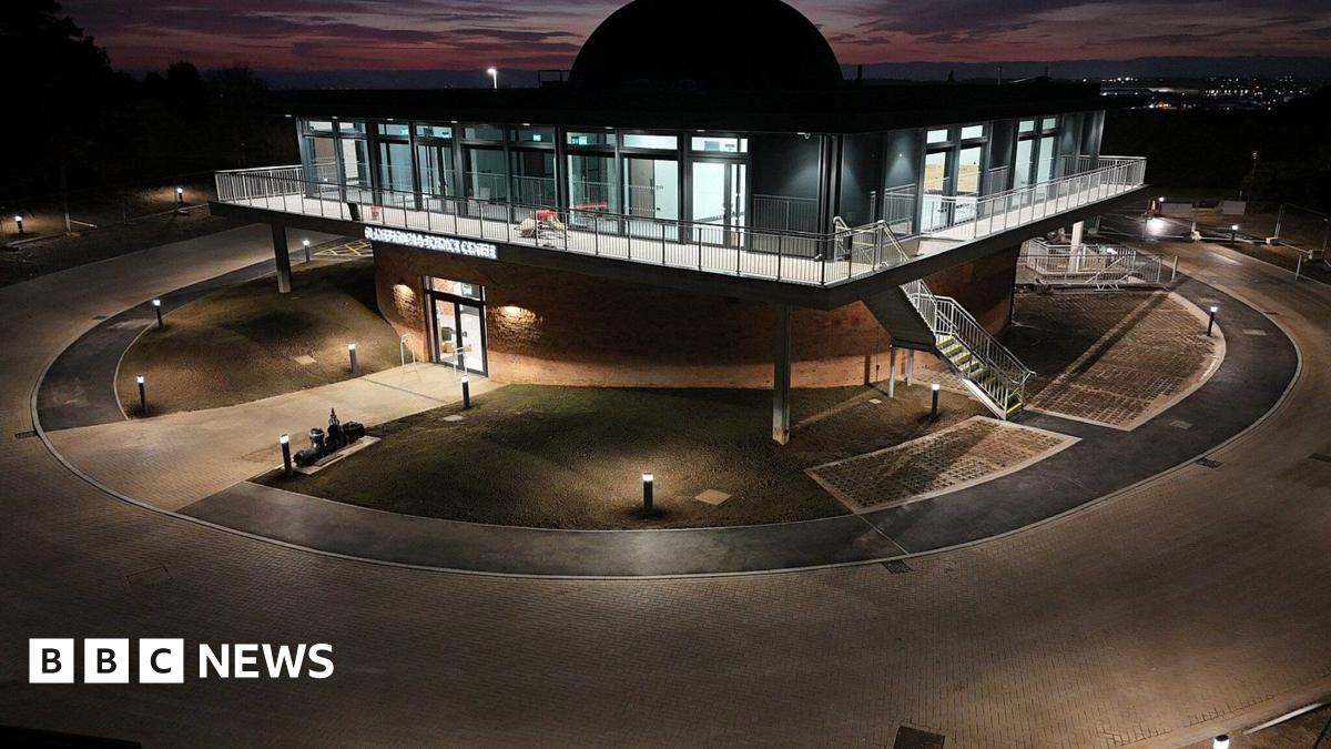The observatory, seen from outside and from an elevated angle, partly flood lit and partly silhouetted against a sunset