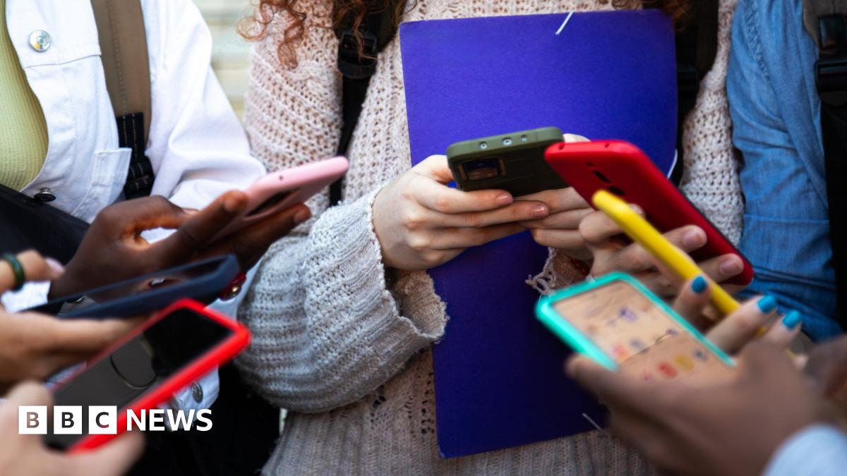 A large number of students stand in a circle on their smart phones in a stock photo. You can only see the hands and blurred phone screens.