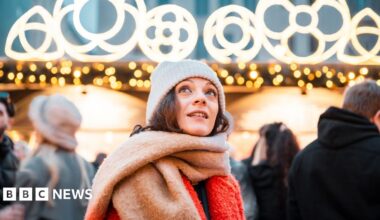 A woman with a white hat brown hair and red and brown scarf.