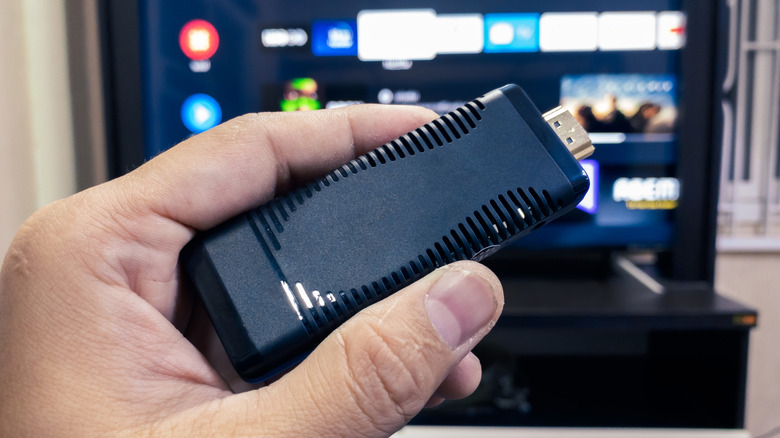A hand holding a USB Drive in front of a TV