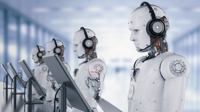 Multiple humanoid robots wearing headsets work at monitors in a row within a futuristic office setting.