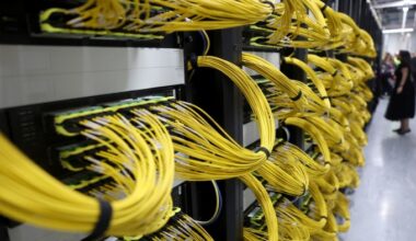 Rows of server racks with dense bundles of yellow network cables inside a data centre.