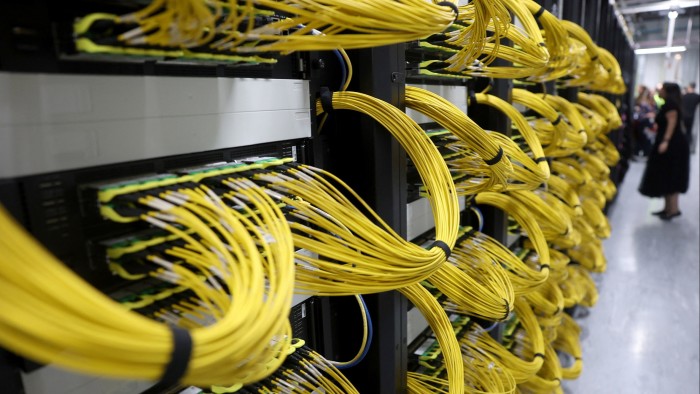 Rows of server racks with dense bundles of yellow network cables inside a data centre.