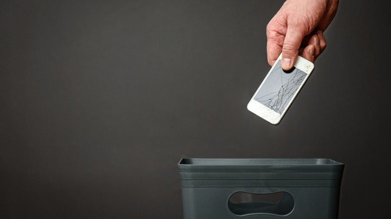 A person throwing out a smartphone in a trash can.