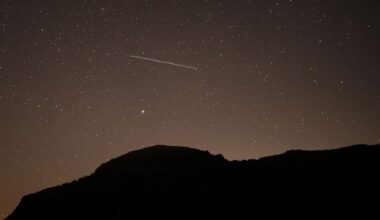 A lone meteor is spotted streaking through a dark starry sky above a silhouetted hill.