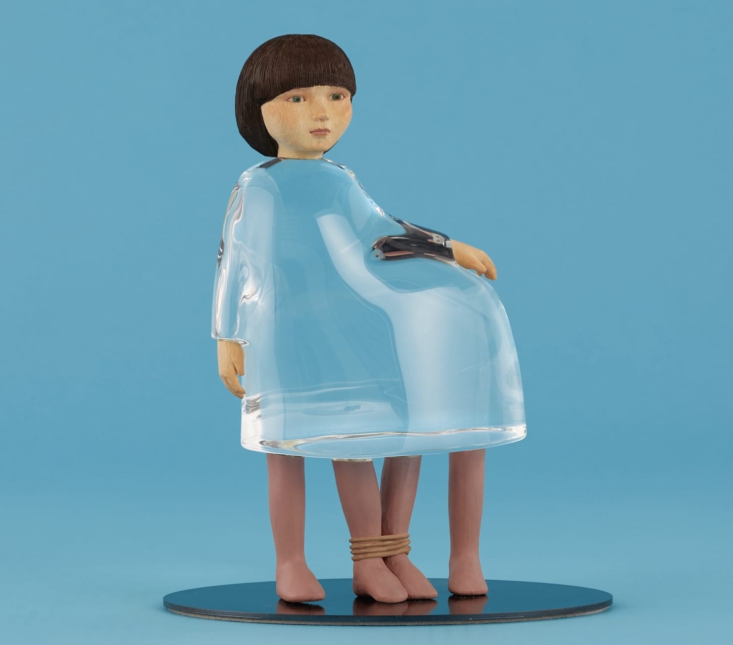 a small sculpture by Ayako Kita made of cypress and acrylic resin, depicting a young woman with a clear dress and an extra pair of legs, with two ankles bound together