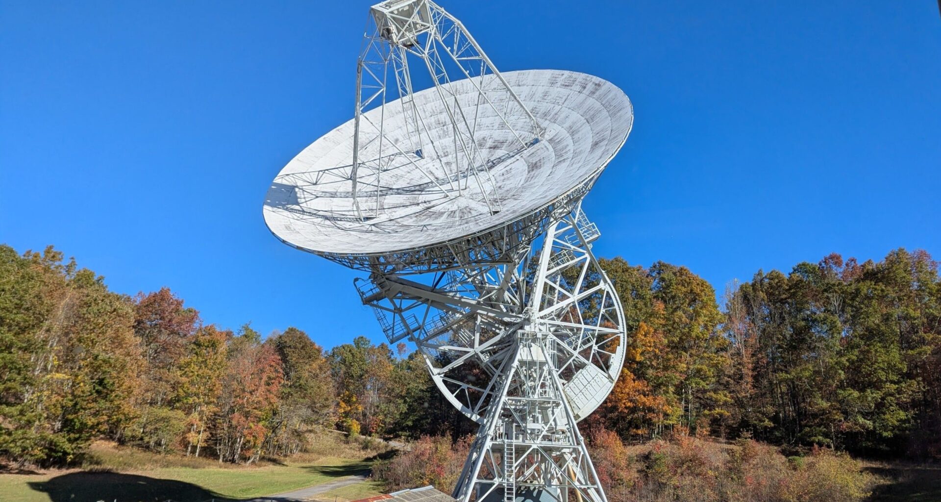 a large white, round antenna surrounded by trees with fall foliage