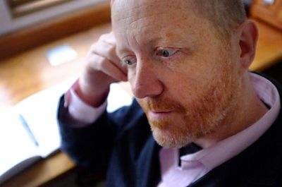 Photo of Michael Symmons Roberts beside a writing desk. 