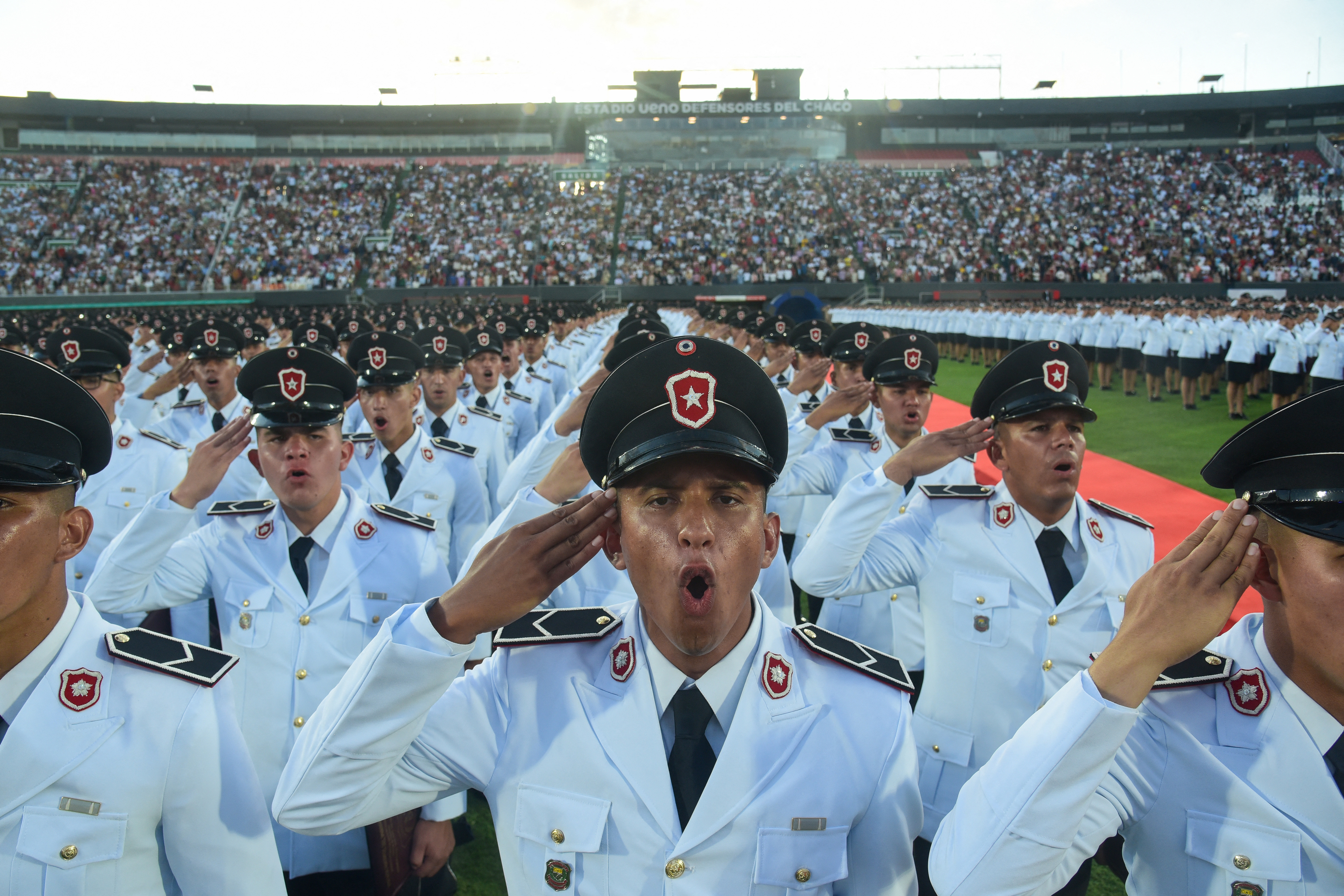 Police officers singing the national anthem and saluting during a graduation ceremony.