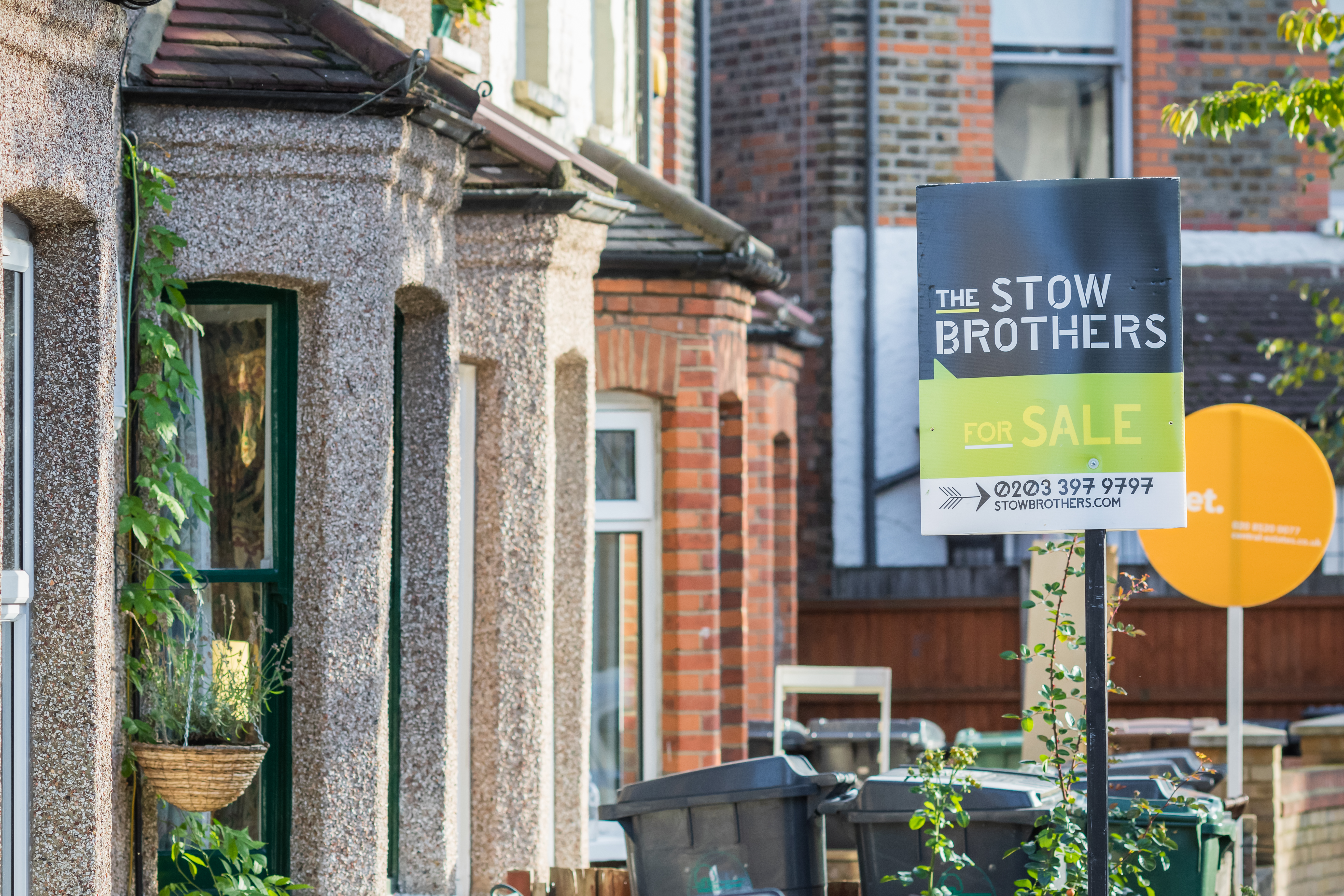 A "For Sale" sign from "The Stow Brothers" estate agency displayed outside terraced houses in Walthamstow, London.