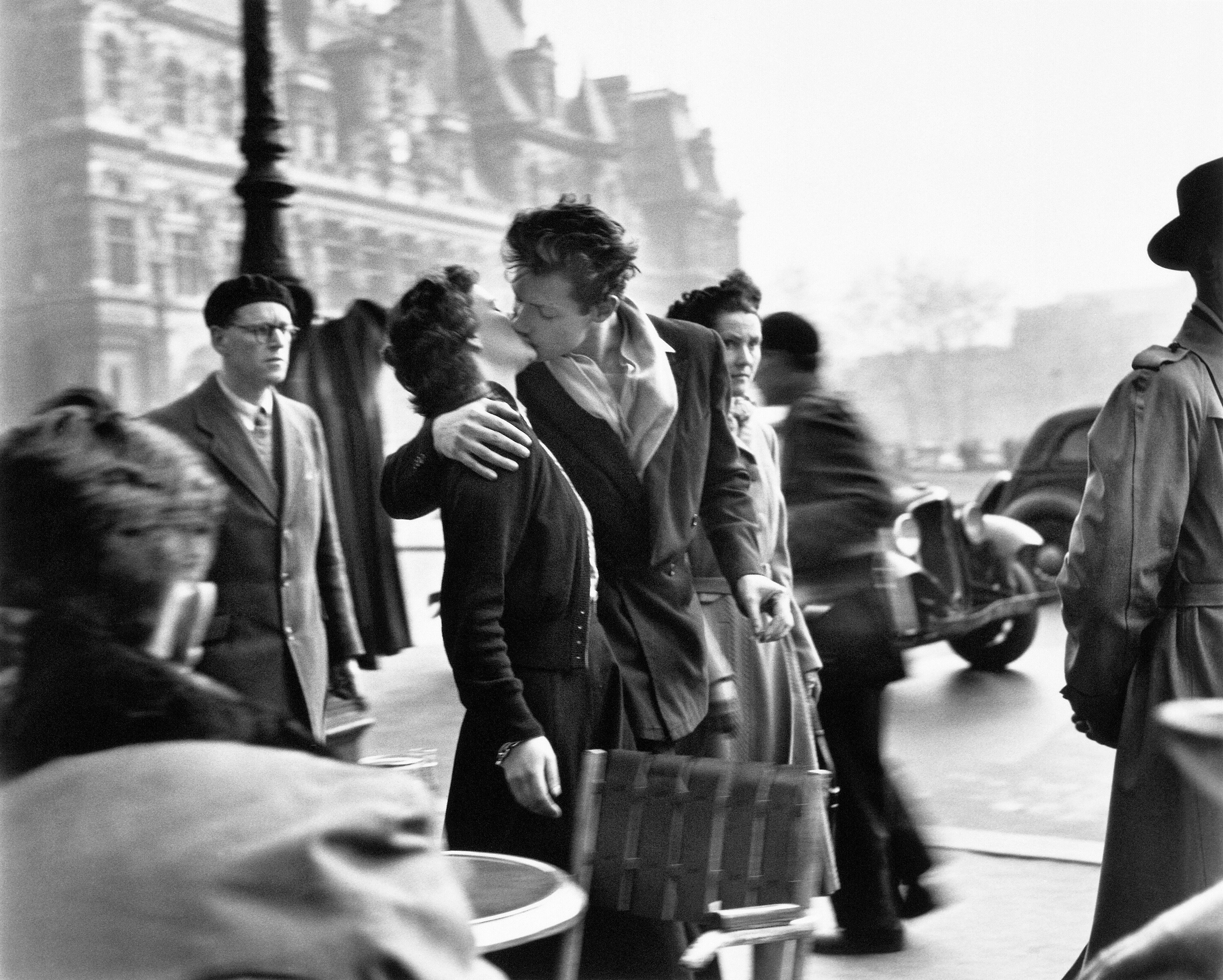 Couple kissing on a street in Paris while people walk by.