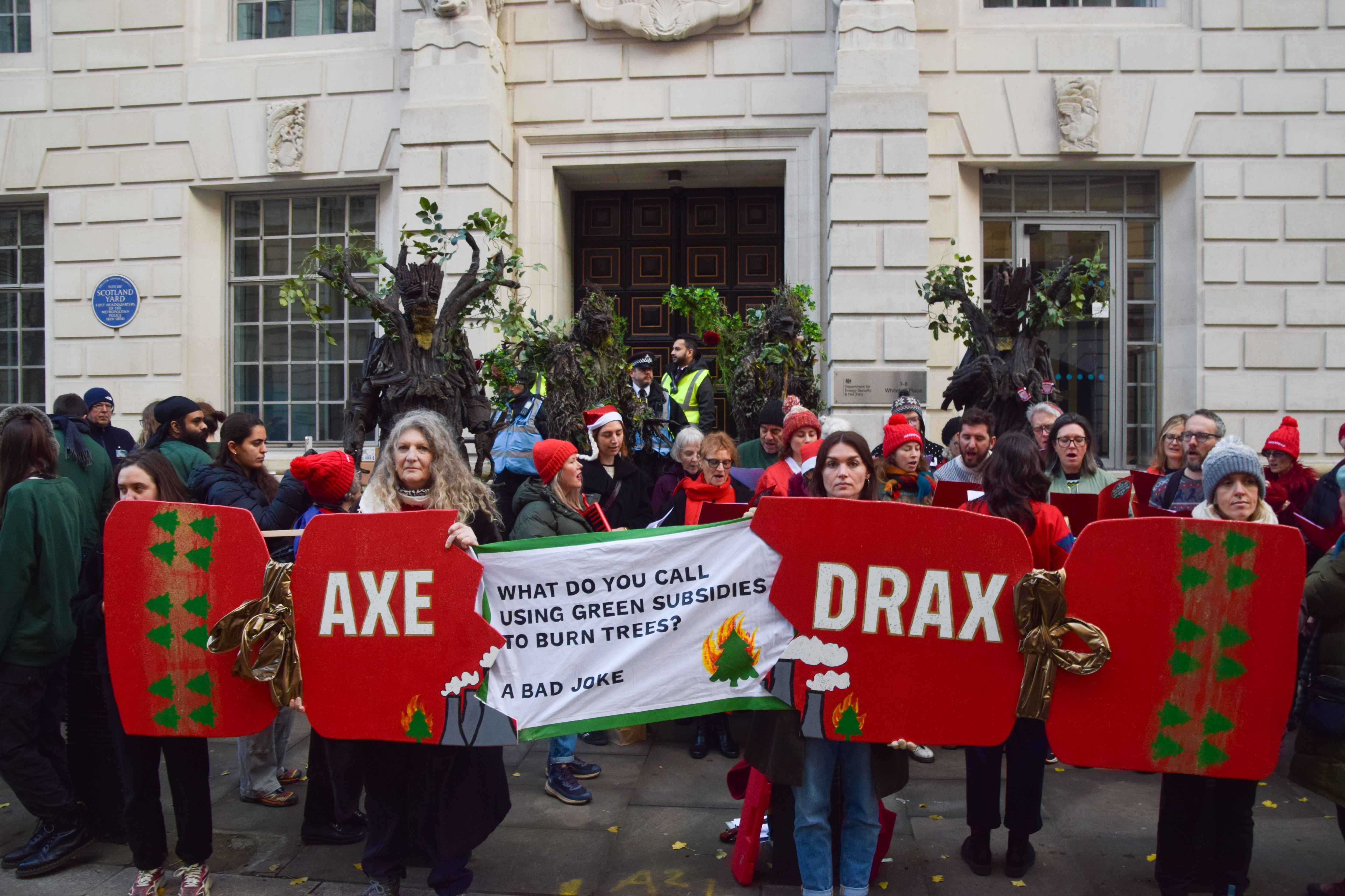 Environmental activists protest Drax, holding a banner and signs shaped like a Christmas cracker that read "AXE DRAX" and "WHAT DO YOU CALL USING GREEN SUBSIDIES TO BURN TREES? A BAD JOKE."