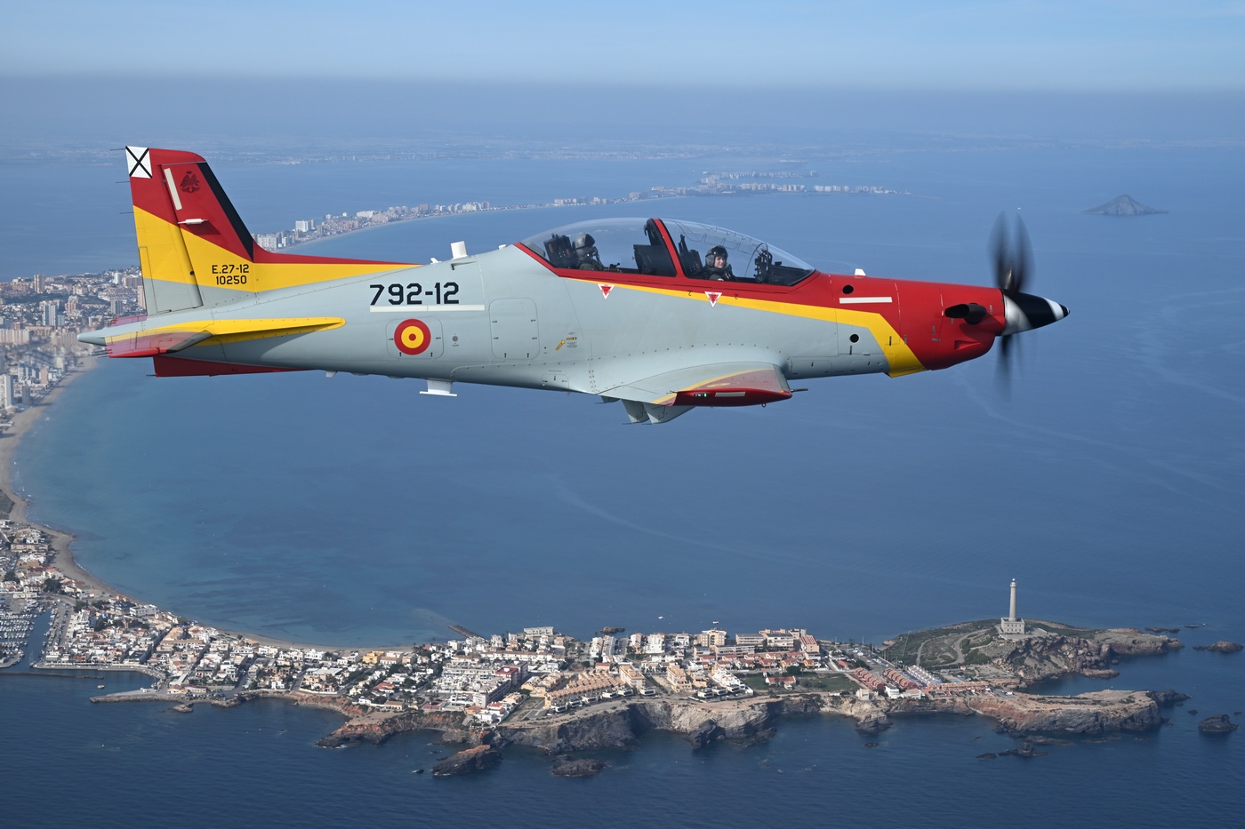 Military training aircraft with Princess of Asturias in cockpit flying over coastal city.