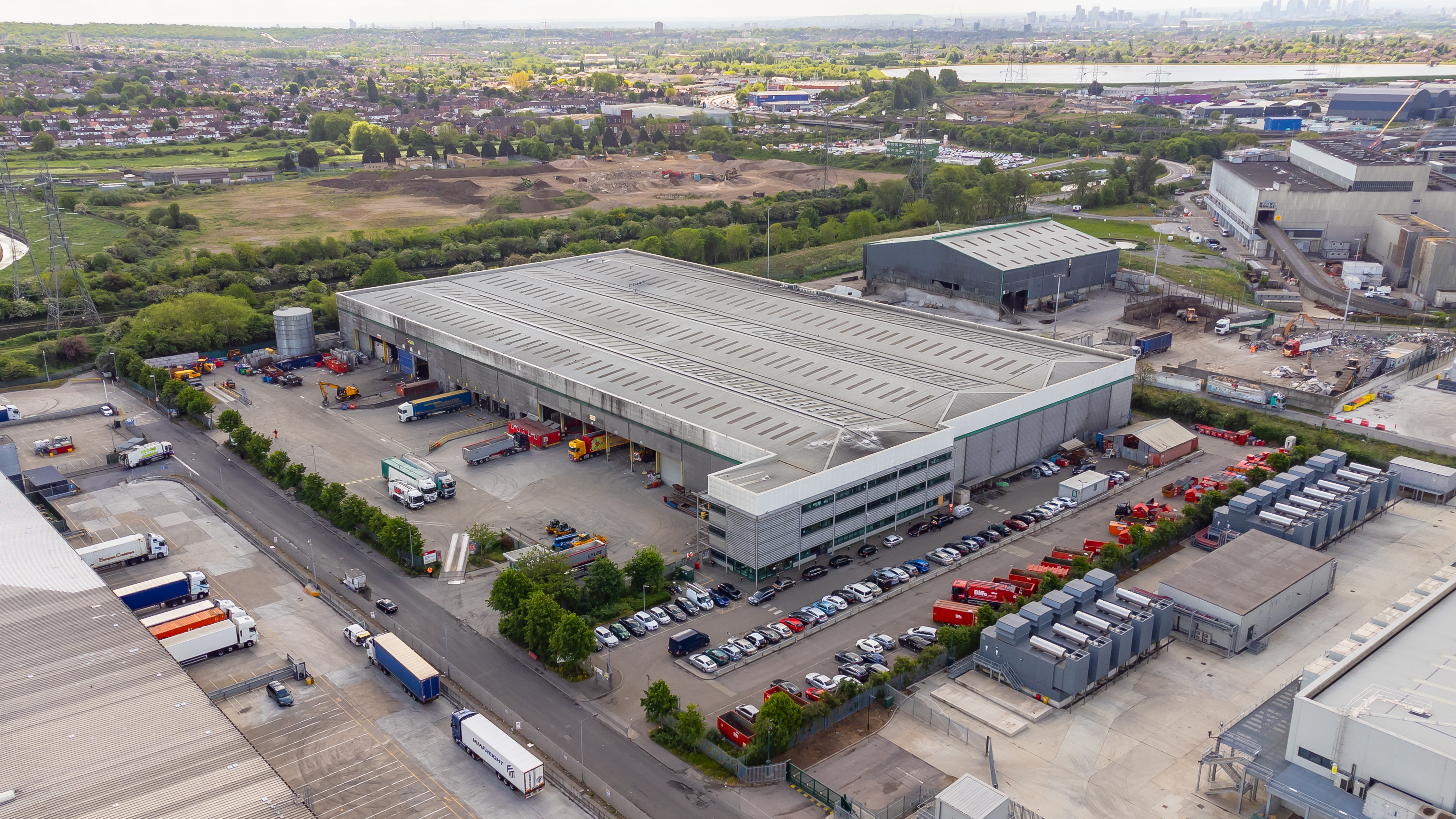 Aerial view of the Biffa Waste Management plant in Edmonton, north London, showing large industrial buildings, parked trucks, and cars, with residential areas and green spaces in the background.