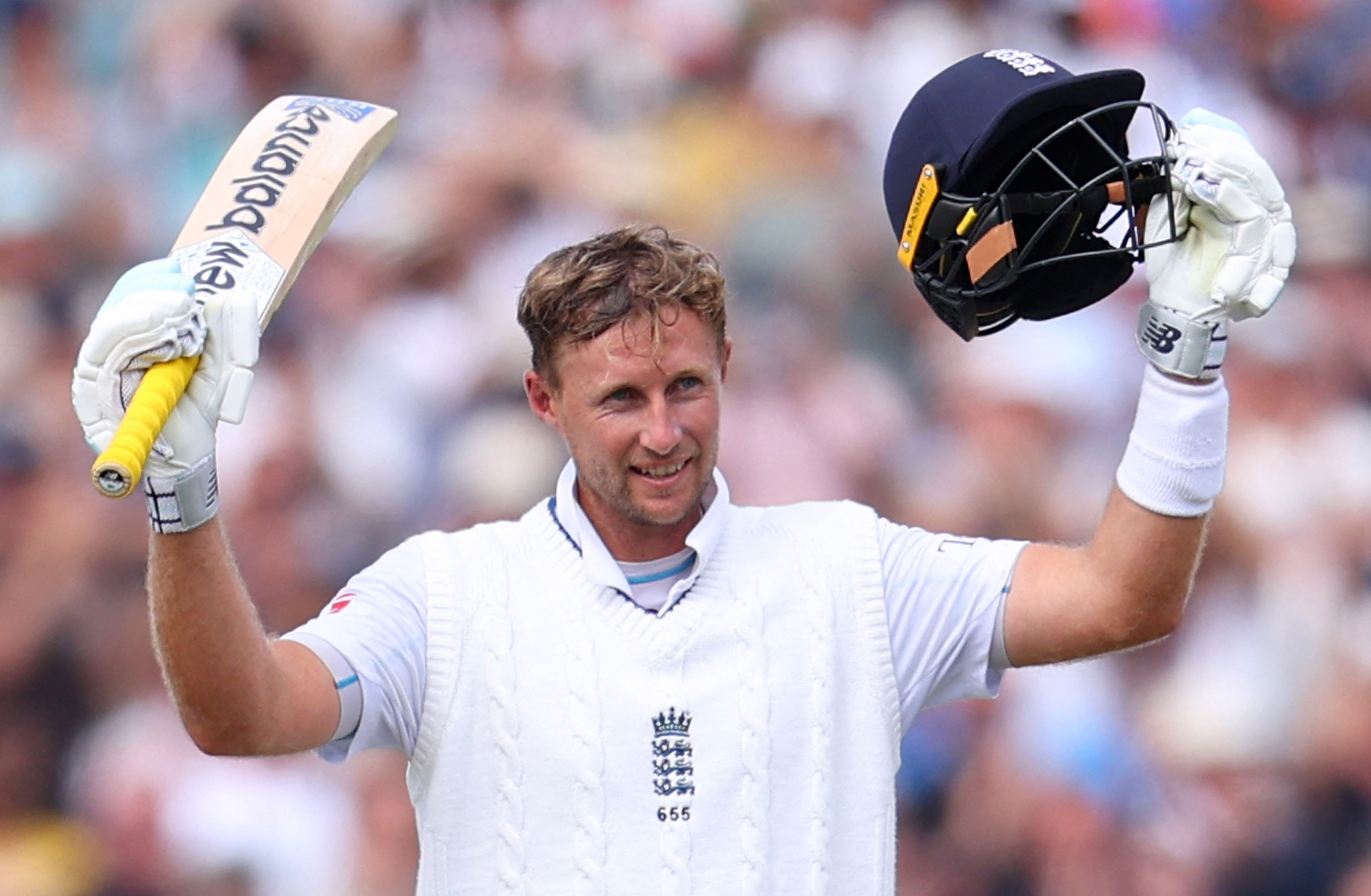 Joe Root celebrating his century, holding a cricket bat and helmet aloft.