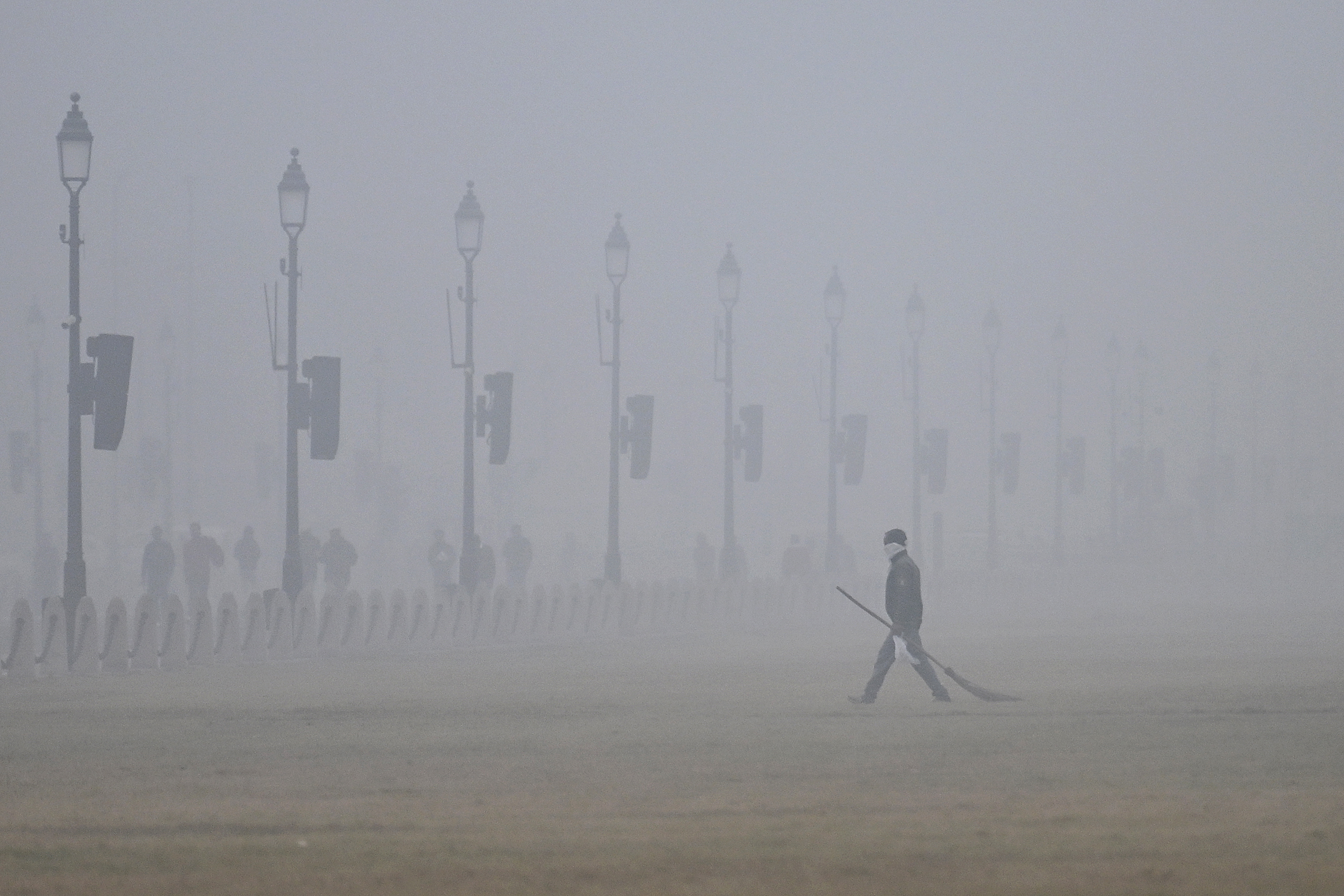 A civic worker with a broom walks along Kartavya Path in New Delhi amid heavy smog.