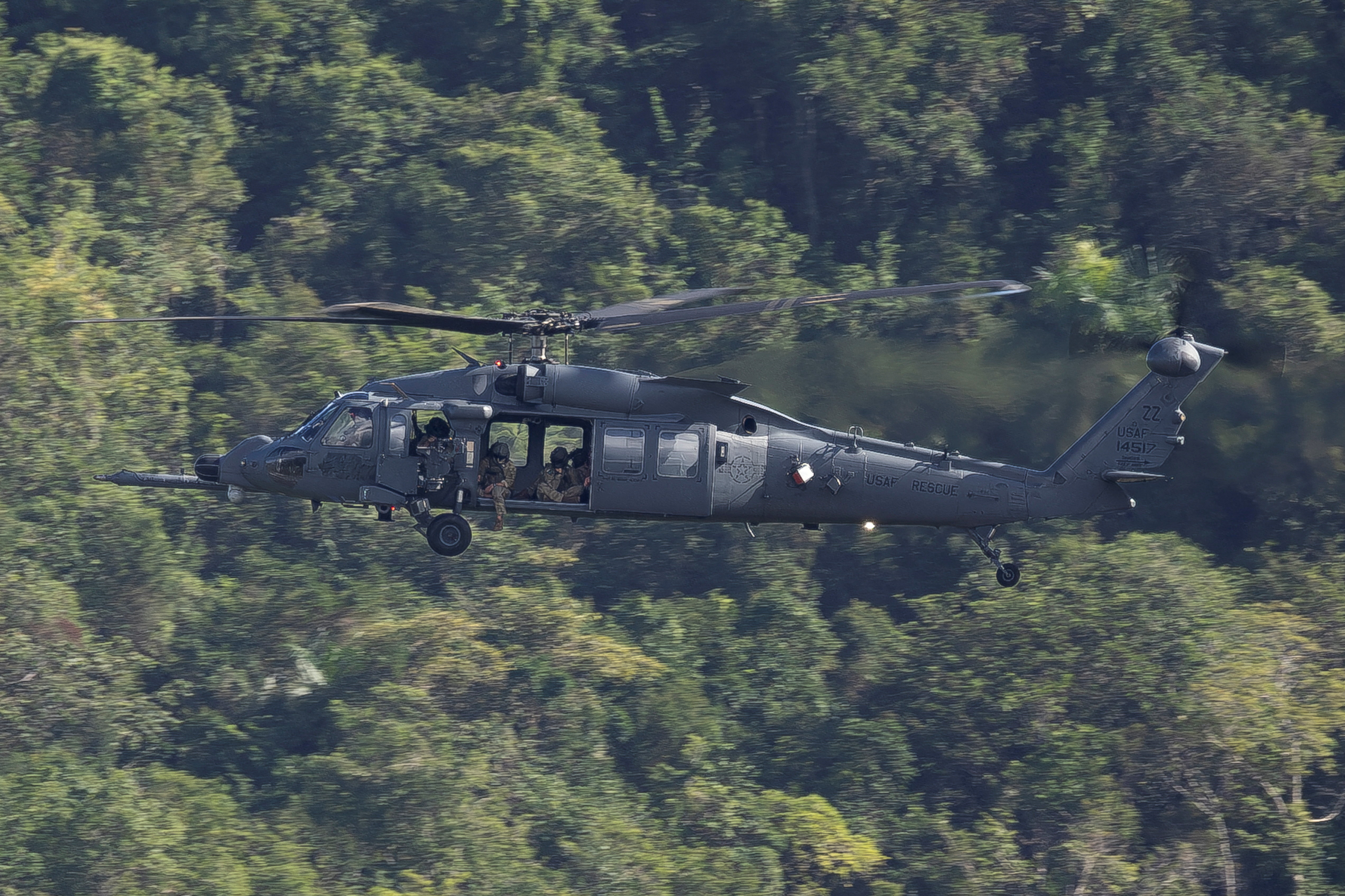 A U.S. Air Force HH-60W Jolly Green II helicopter flying over green trees in Ceiba, Puerto Rico.