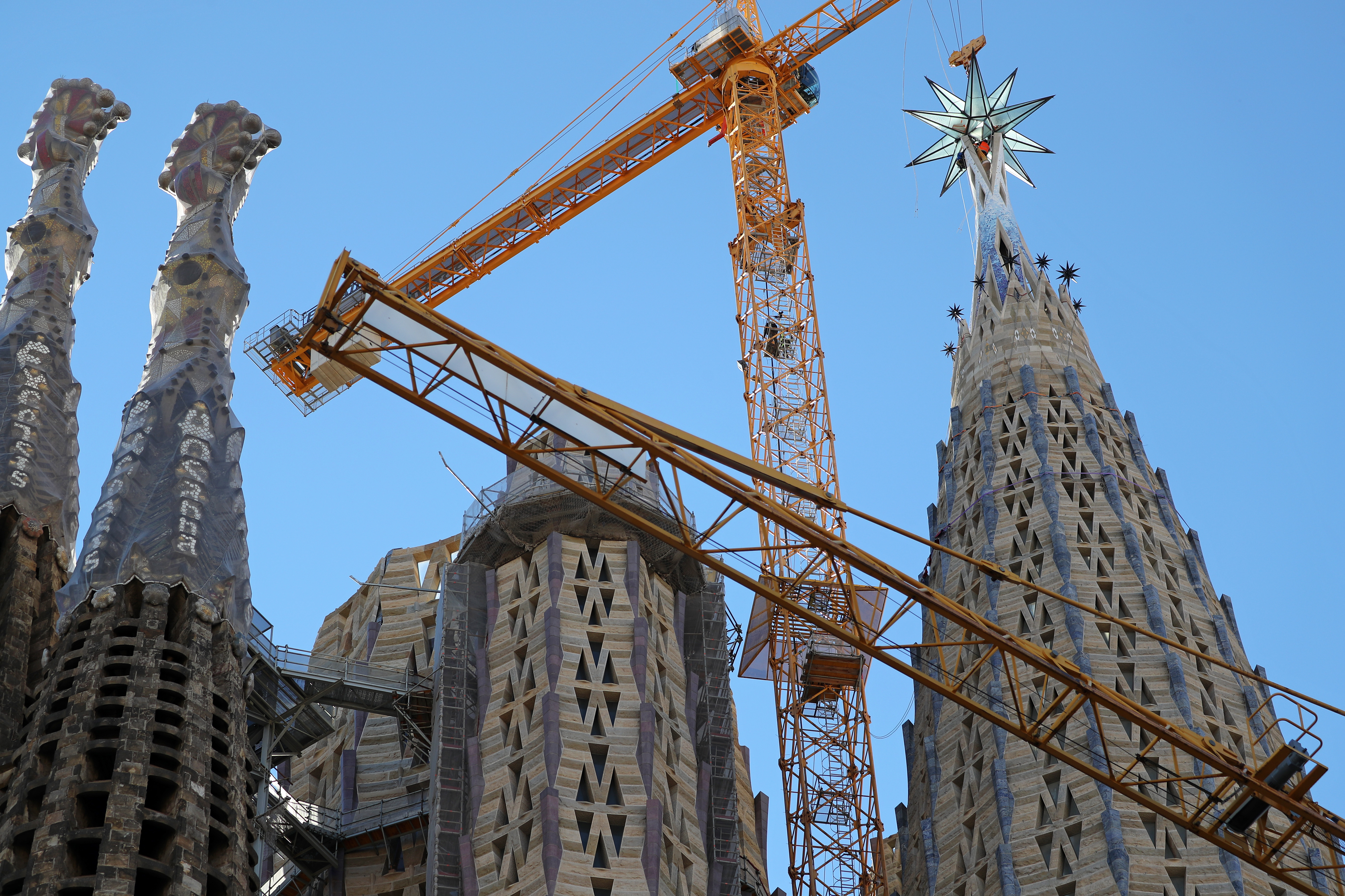 Two large towers of the Sagrada Familia with an orange construction crane in front, placing a star on the rightmost tower.