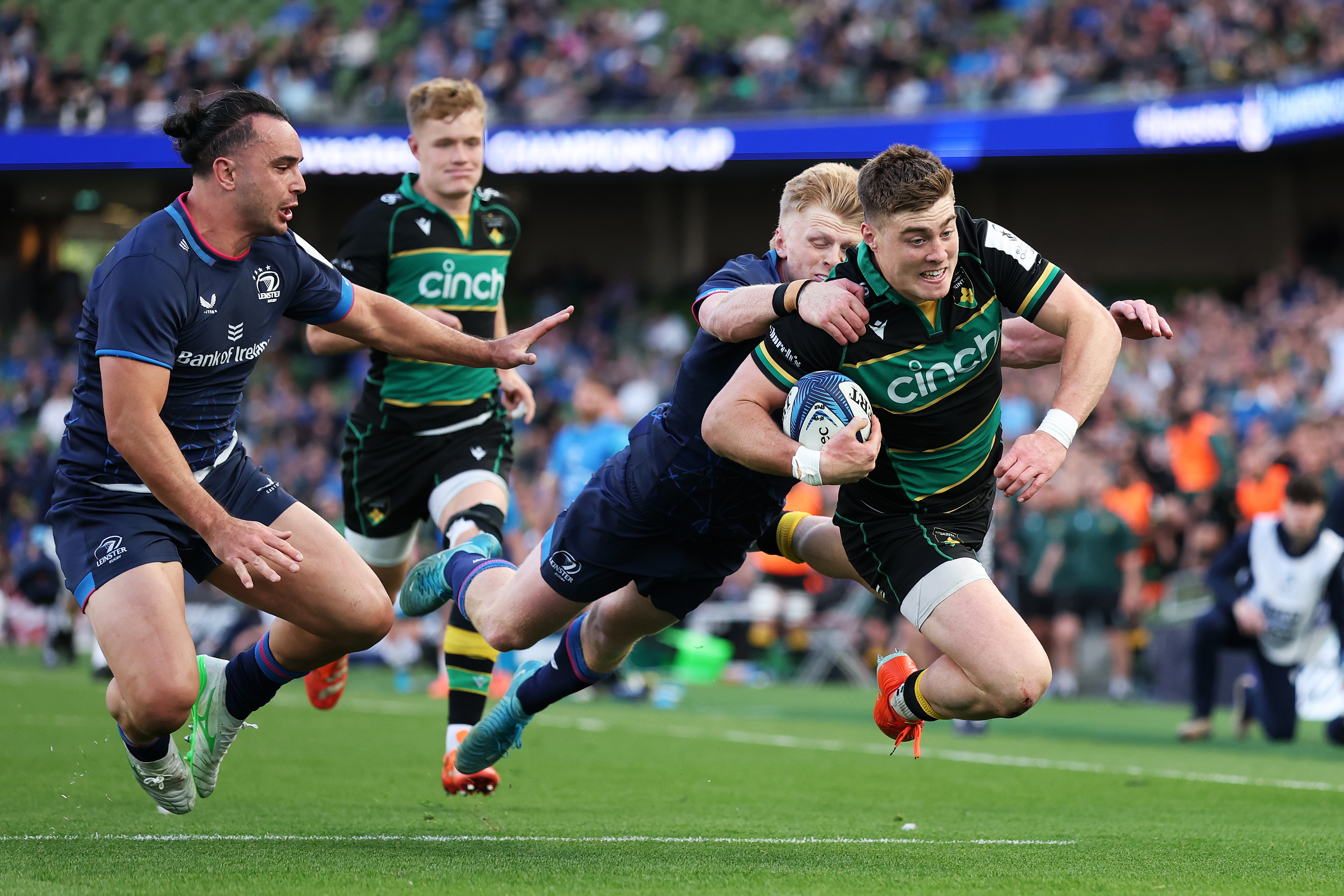Tommy Freeman of Northampton Saints scores his team's fourth try, diving while being tackled by James Lowe and Tommy O'Brien of Leinster.