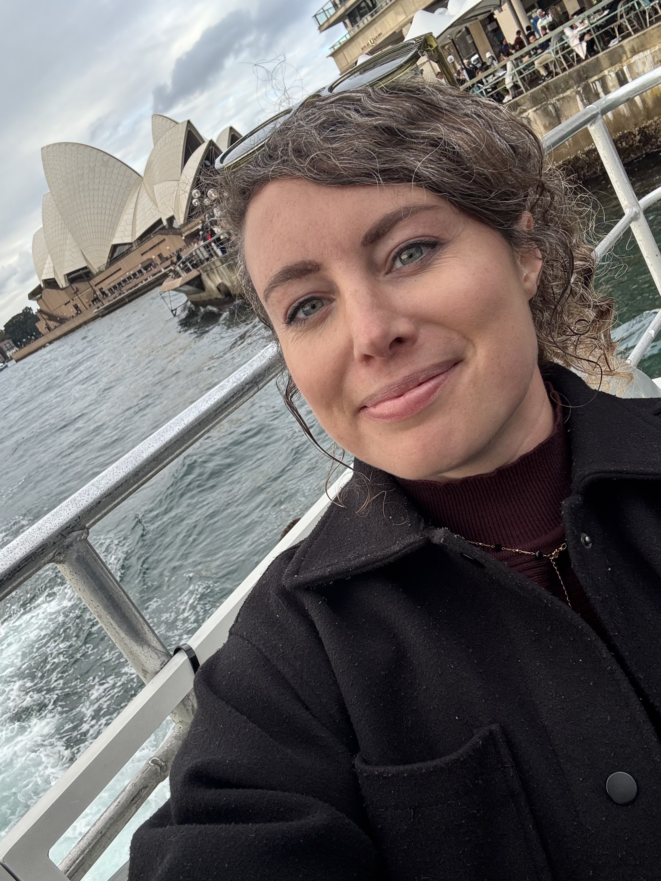 Lizzie Davey in Australia, smiling from a boat with the Sydney Opera House in the background.