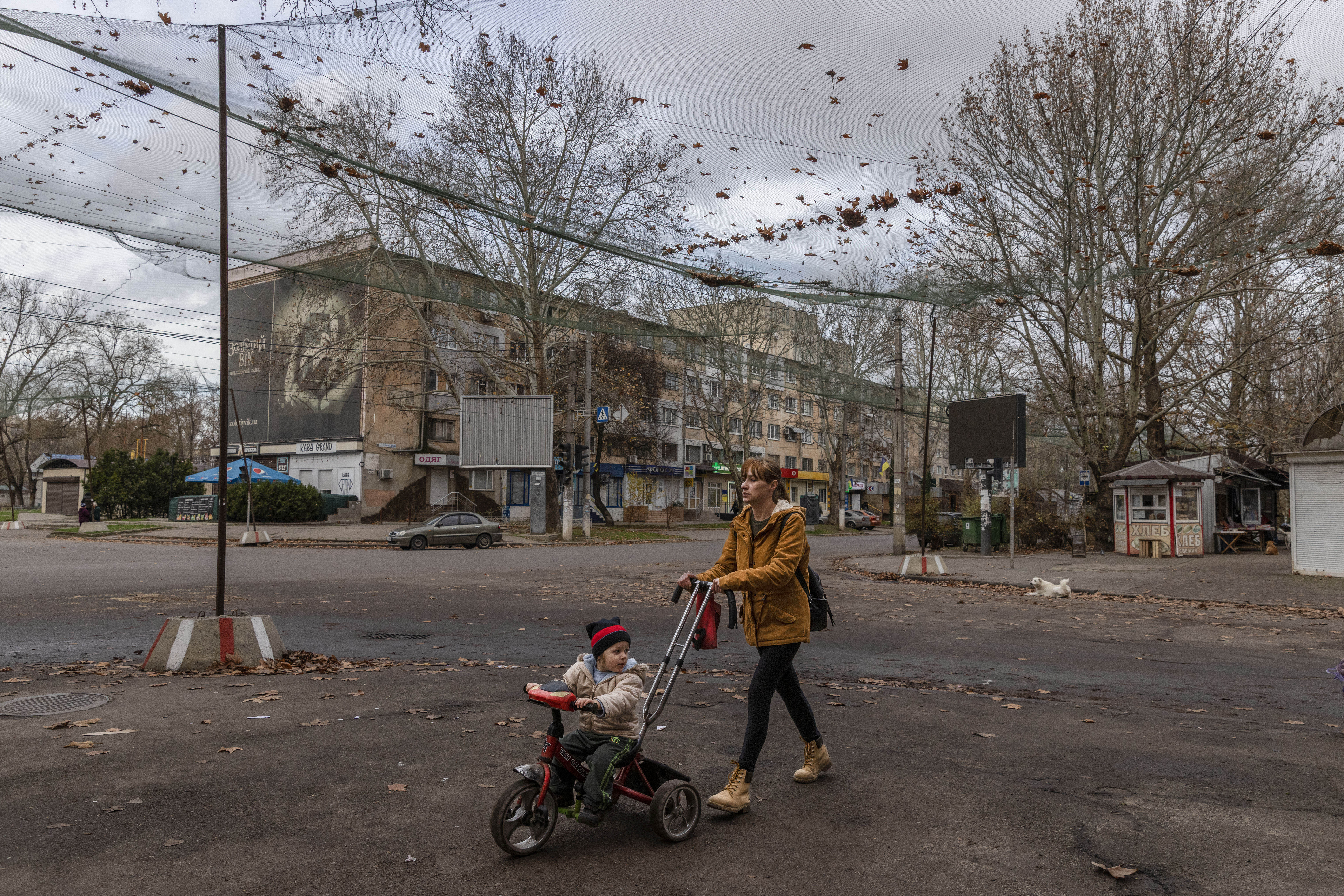 Illiushy Kulyka Street in Kherson, covered with anti-drone netting, with a woman pushing a child on a tricycle.