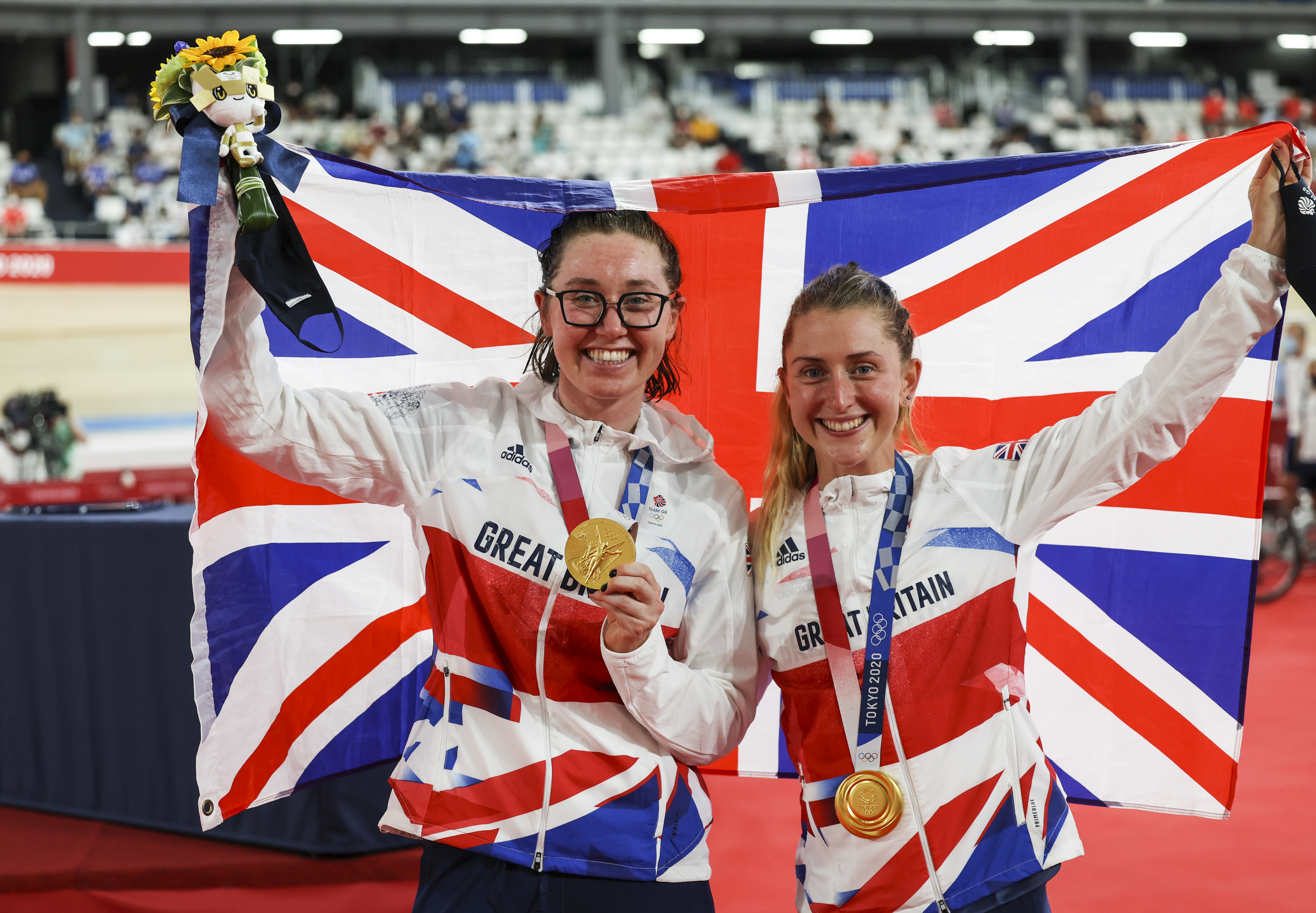 Katie Archibald and Laura Kenny of Team Great Britain celebrating their gold medal win, holding the Union Jack flag and their medals.
