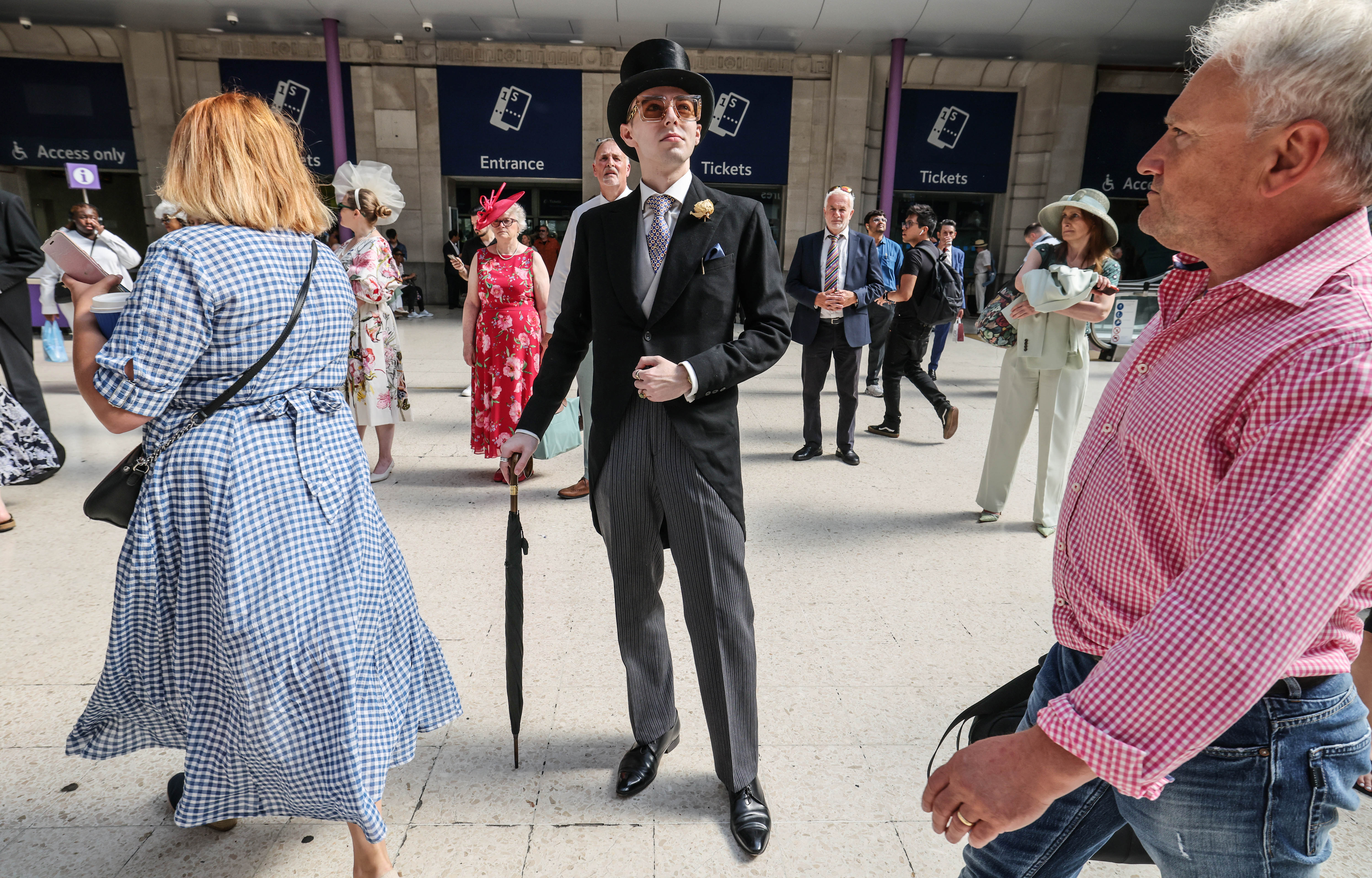 A smartly dressed gentleman stands in Waterloo train station looking up at the notice board for trains to Ascot.