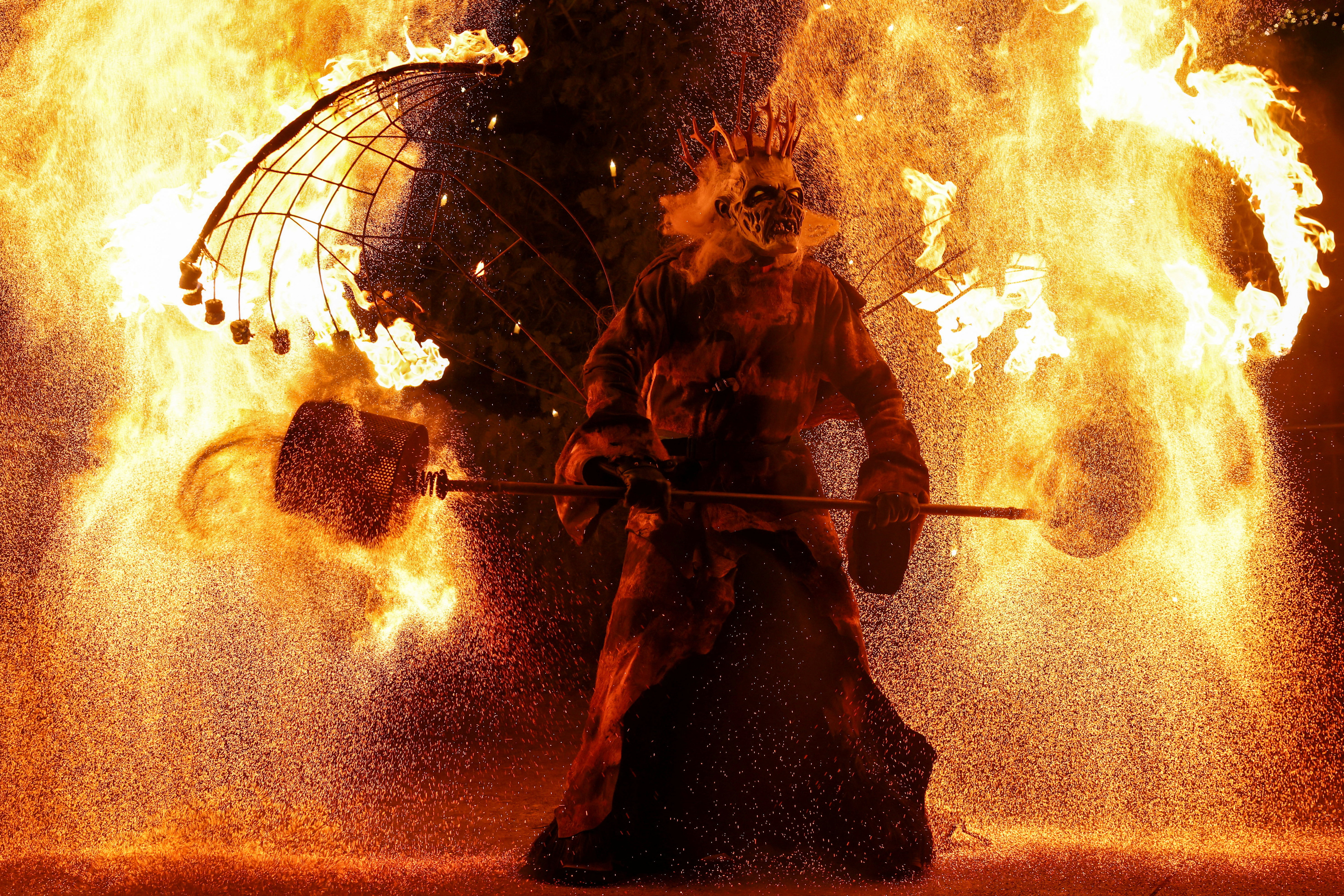Performer in a costume, holding a staff, participates in the traditional Rauhnacht run during "The Twelve Nights of Christmas" in Beilngries, Germany, surrounded by fire and sparks.