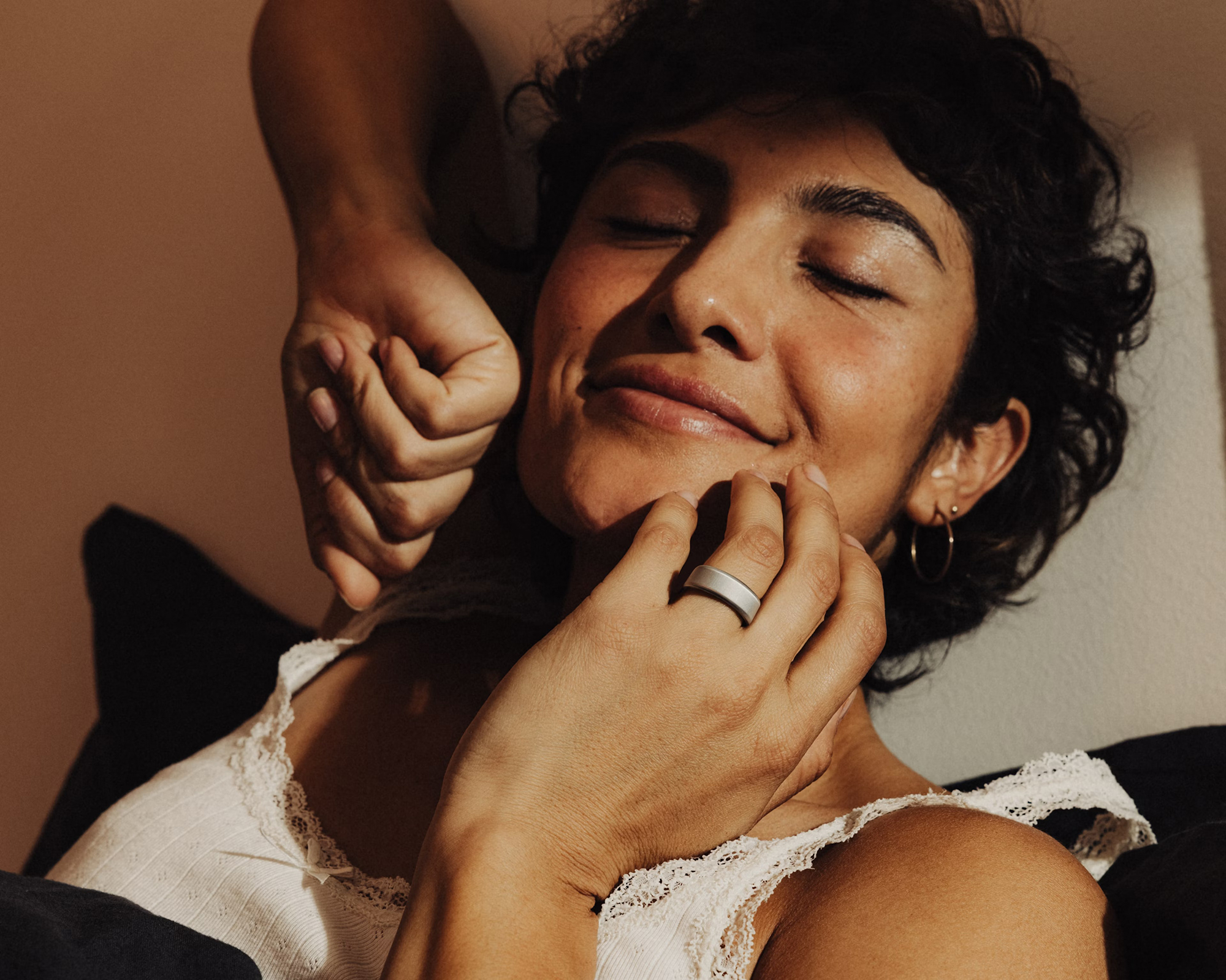A woman with curly hair smiles with her eyes closed as she wears a gray smart ring.