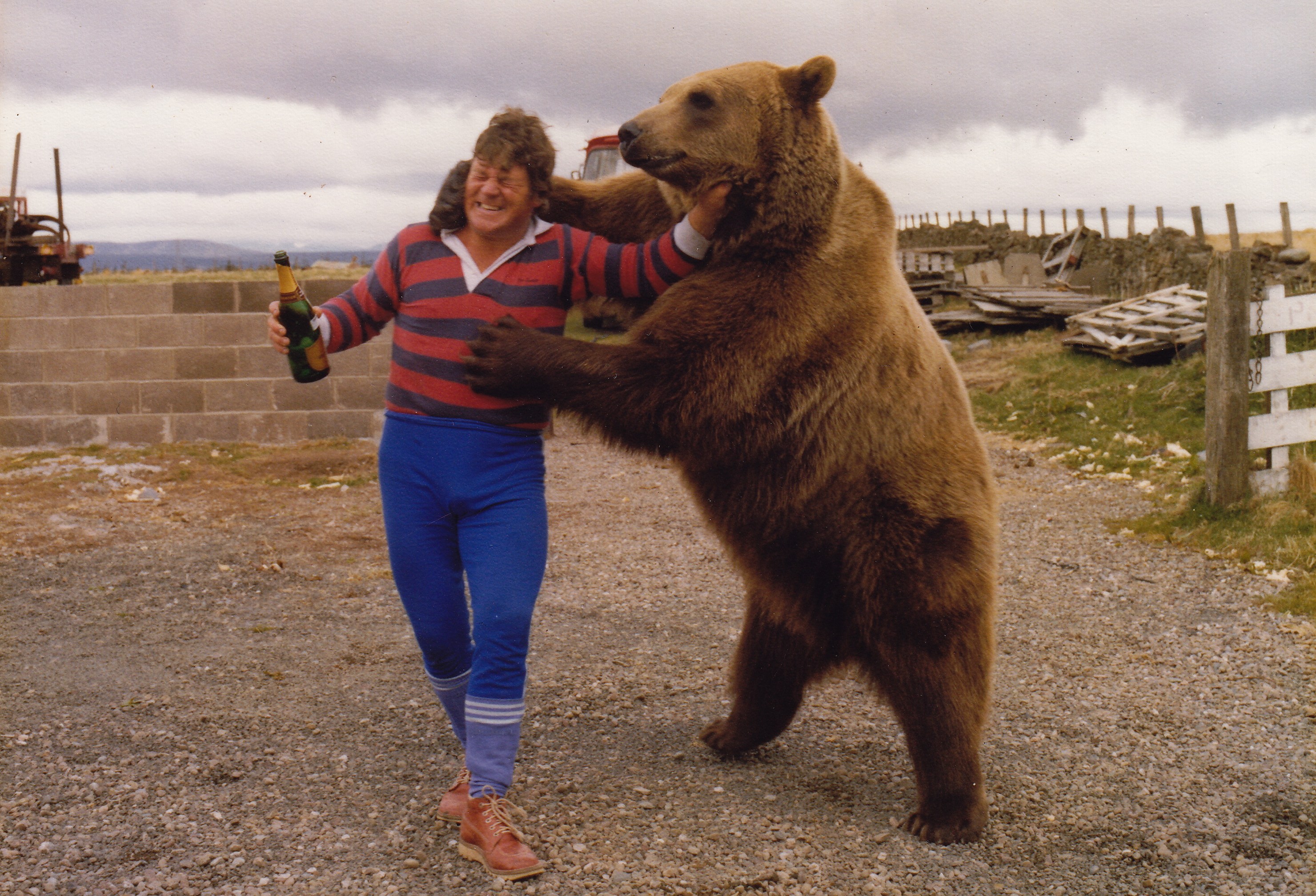 Andy Robin holds a bottle of champagne while Hercules the Bear playfully puts his paw around Robin's neck.