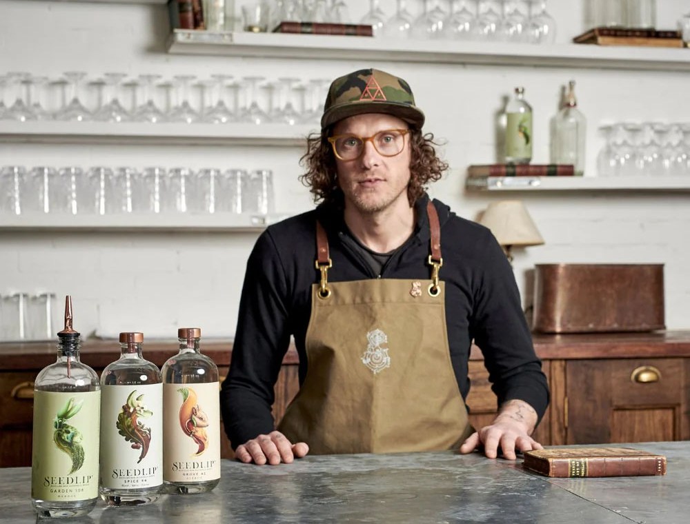 Ben Branson, CEO of Seedlip, standing behind a bar with three Seedlip bottles.