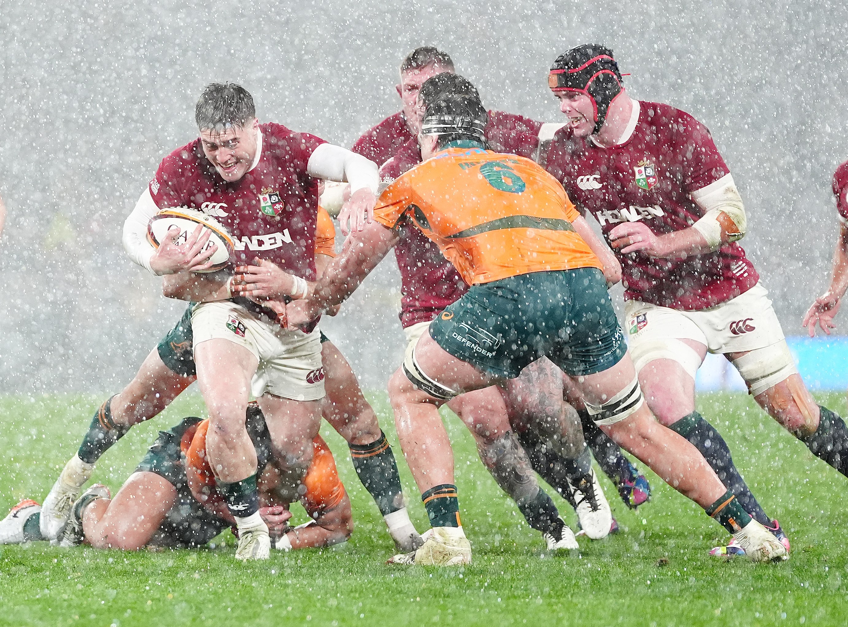 British and Irish Lions' Tommy Freeman carries the ball during a rugby match in the rain.