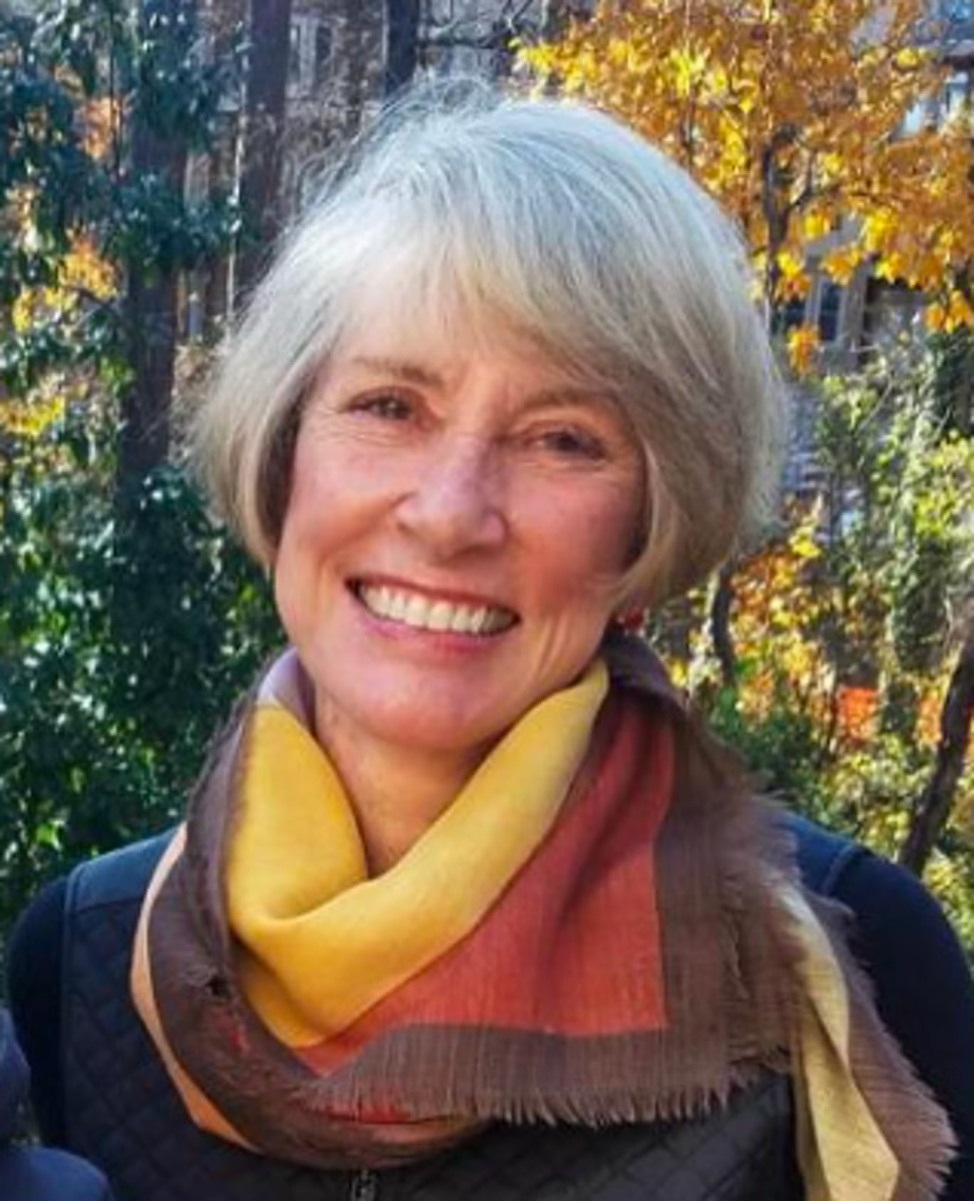 Suzanne Adams, a woman with short gray hair and a colorful scarf, smiling.