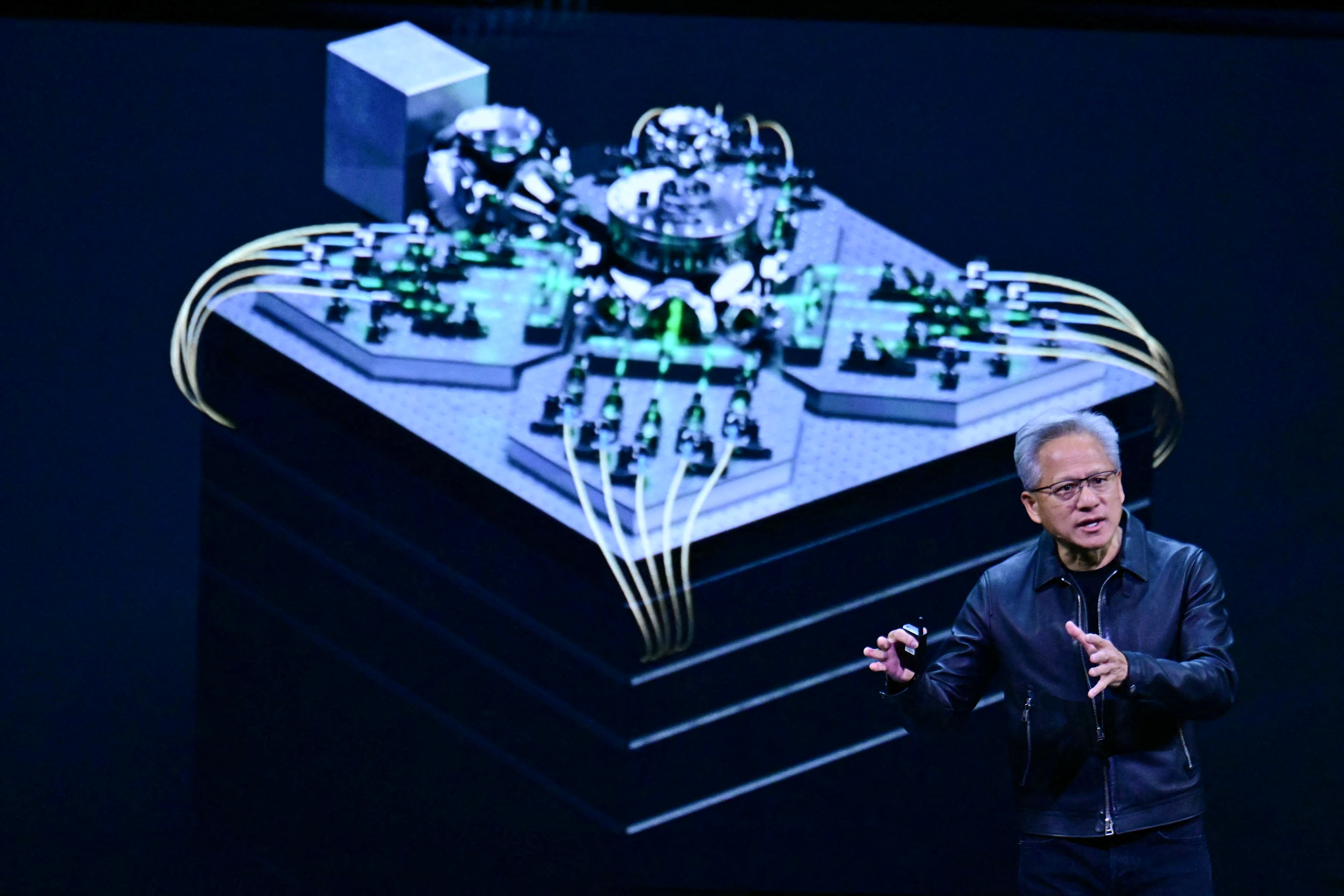 NVIDIA CEO Jensen Huang speaking at the GTC conference with a large graphic of a microchip on a screen behind him.