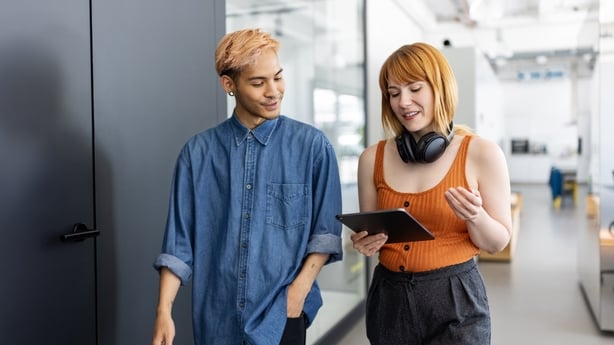 Startup business partners walking through office corridor using digital tablet and discussing work. Businesswoman looking at digital tablet and talking colleague at work.