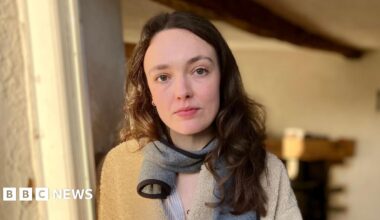 Amelia is standing in her doorway, with her empty front room behind her.