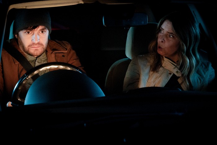 Charity looks shocked, staring at Mack who is furiously clinging to the steering wheel in a scene from Emmerdale
