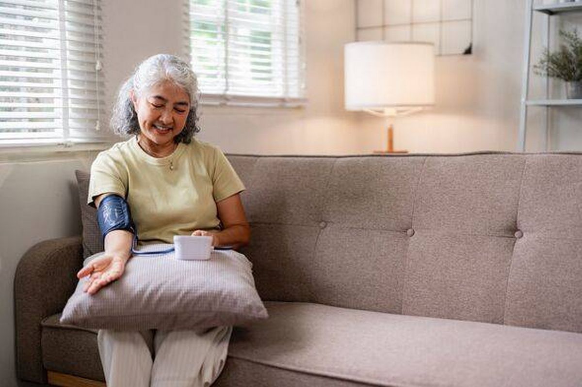 Asian senior woman measures blood pressure home self care wellness routine comfortable living room